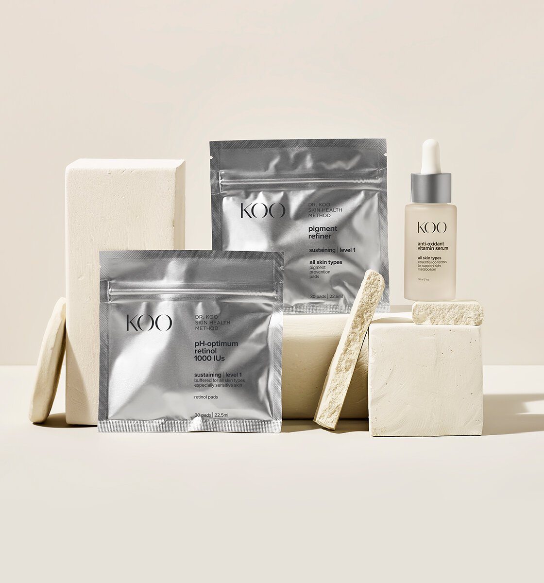 Skincare products, including retinol patches, pigment refiner, vitamin serum, and cleansing bars, arranged on white geometric blocks.
