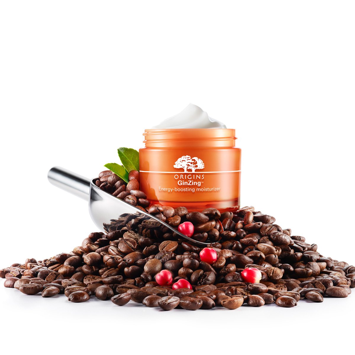 A jar of Origins GinZing energy-boosting moisturizer placed on a pile of coffee beans with a scoop and some red berries around it.