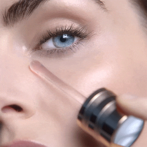 A close-up of a person applying eye serum with a dropper to the area below their eye.