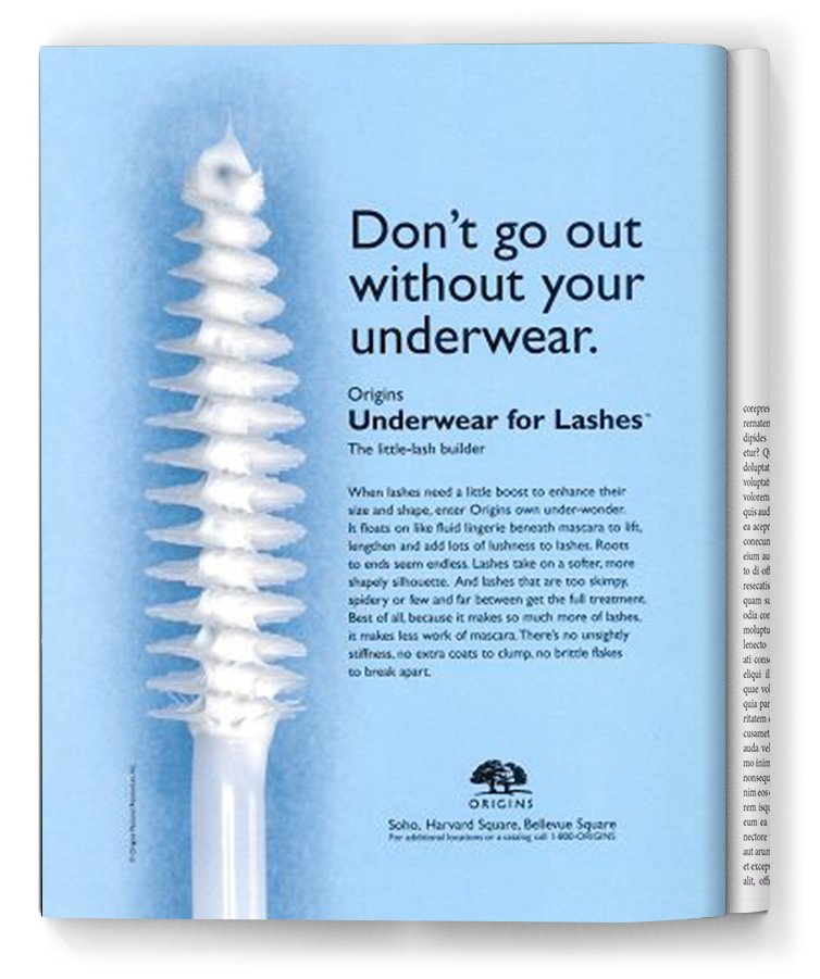 Magazine page featuring a white mascara spoolie brush and a blue background with text about under eye makeup and eyelashes from the brand Origins.