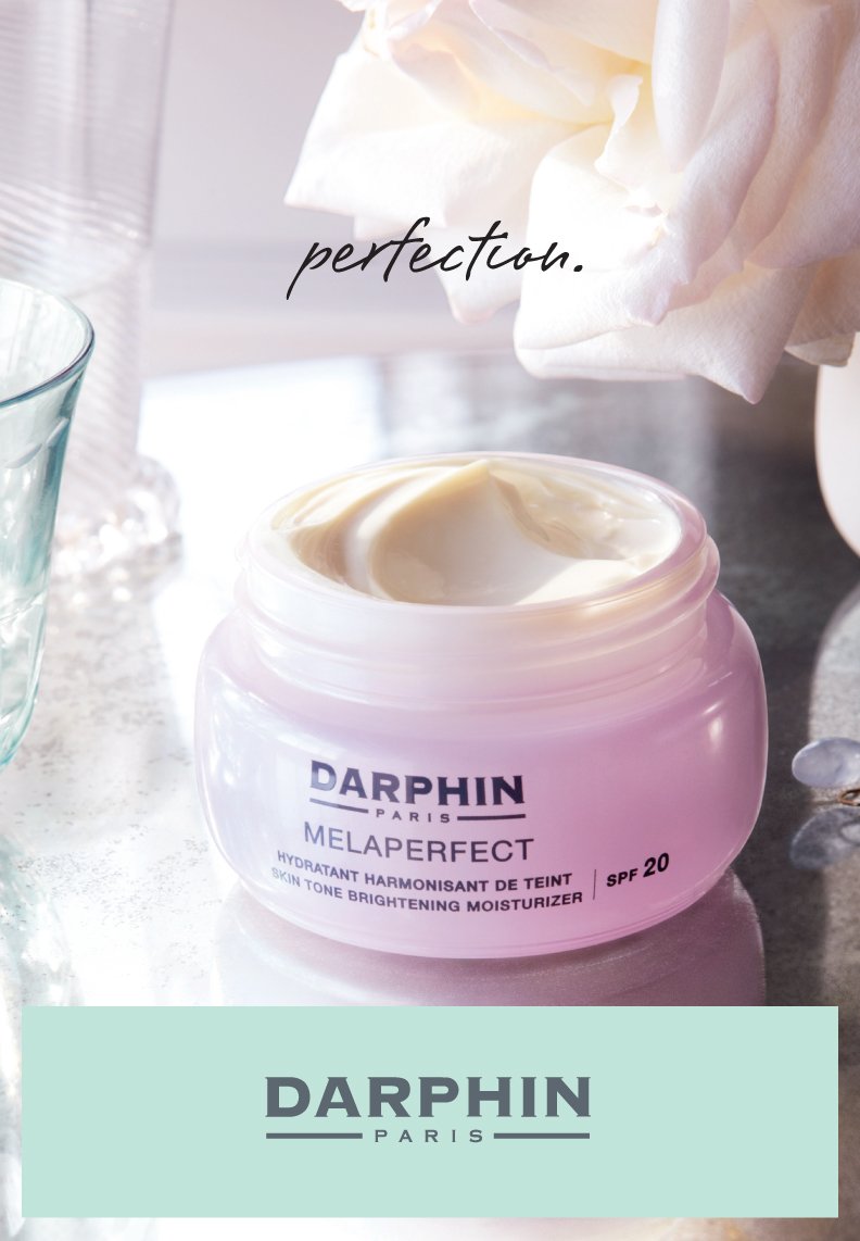 A pink jar of Darphin Paris Melaperfect brightening moisturizer with SPF 20 on a white surface, with soft natural light and a crumpled tissue paper in the background, and the word 'perfection' written above.