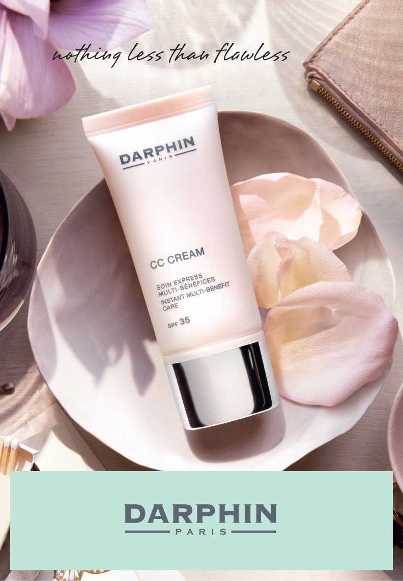 A tube of Darphin CC Cream SPF 35 on a white dish with rose petals. The background includes a partial pink flower, a beige pouch, and a soft-colored surface with the phrase 'nothing less than flawless' written at the top.