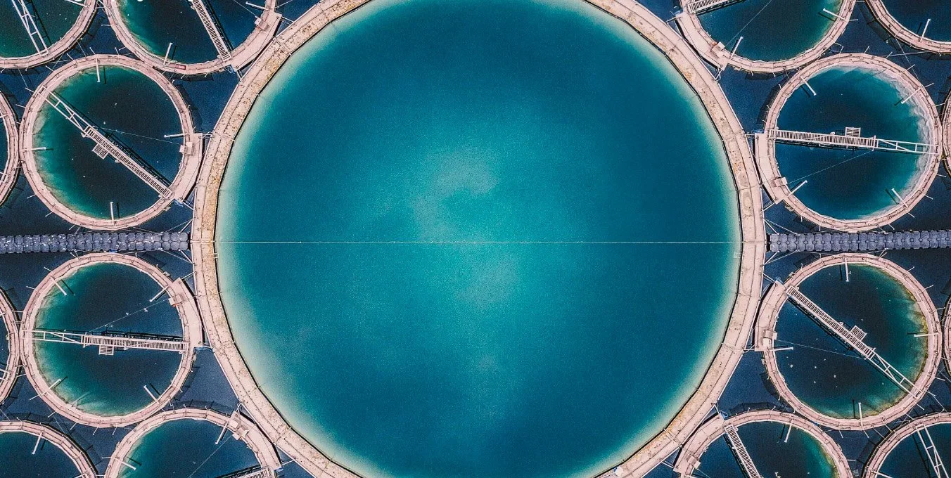 Aerial view of water treatment tanks arranged in a circular pattern, with a large central tank and smaller surrounding tanks.