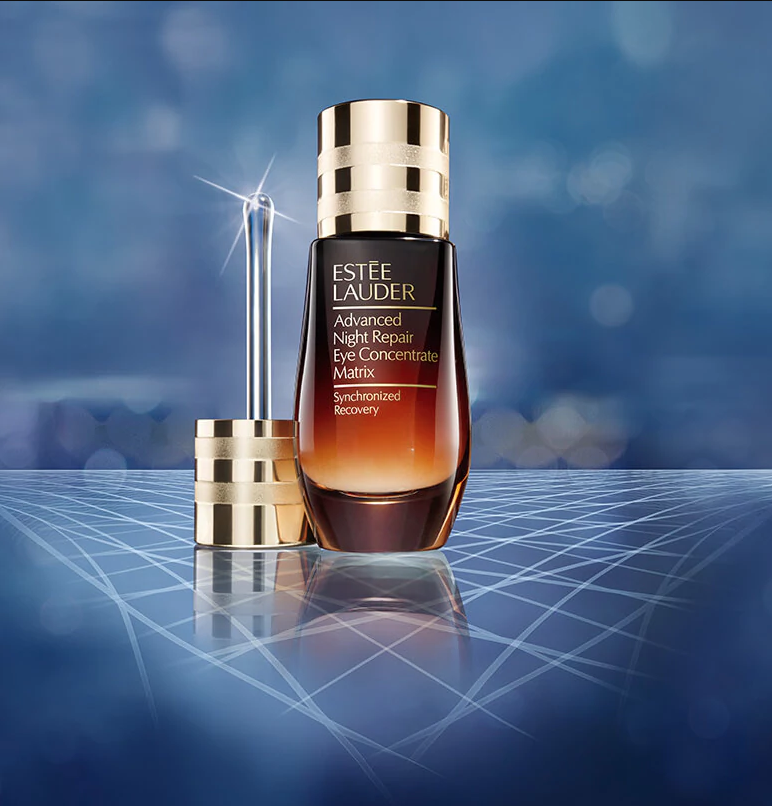 A bottle of Estée Lauder Advanced Night Repair Eye Concentrate Matrix with applicator wand against a blue, futuristic background.