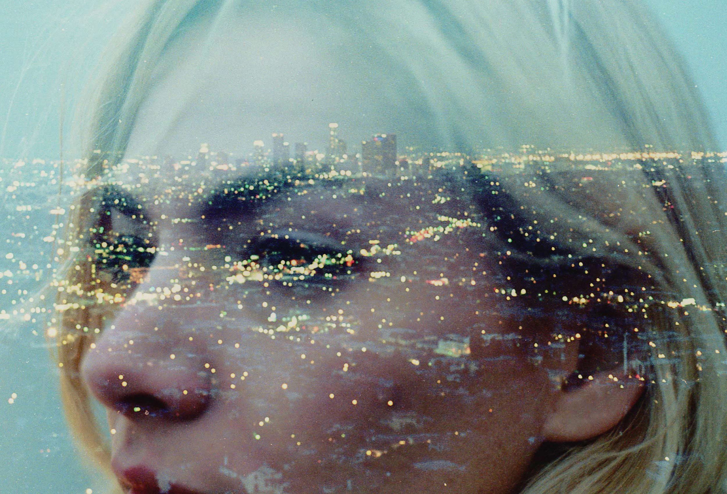 A woman's face merges with a cityscape at night, creating a double exposure effect.