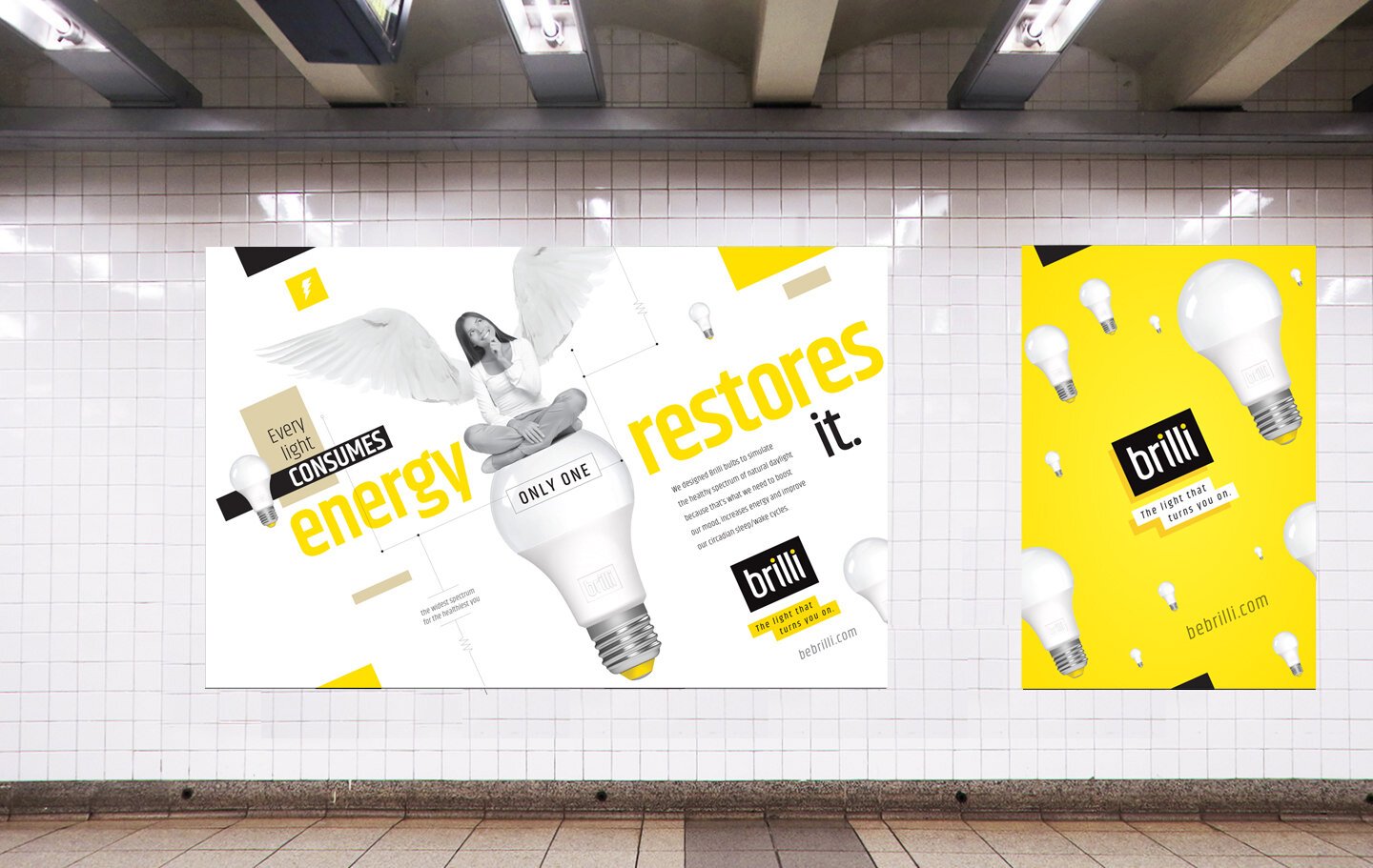 Two advertisements for light bulbs on a tiled wall in an underground transit station. The left ad features a woman with angel wings sitting atop a large light bulb, with bold yellow and black text that reads "Energy restores". The right ad has a yell
