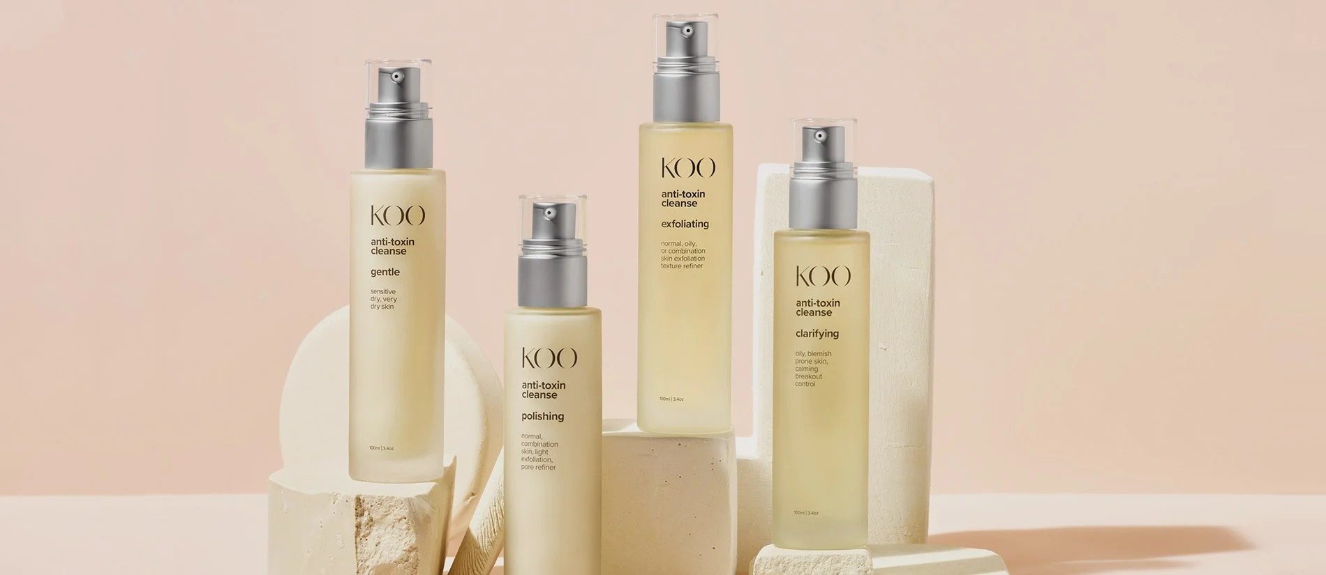 Collection of KOI skincare bottles with pump dispensers in light yellow color, set against pastel pink background, with some bottles placed on white blocks and textured surfaces.